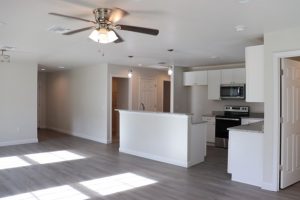 Bright, modern kitchen and living space with white cabinetry and ceiling fan.
