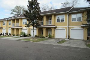 A row of modern yellow townhouses with garages and small front yards.