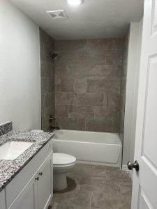 A modern bathroom with granite countertop and tiled bathtub area.