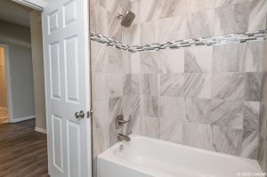 Clean bathtub with marble-style tiled walls and a modern showerhead.